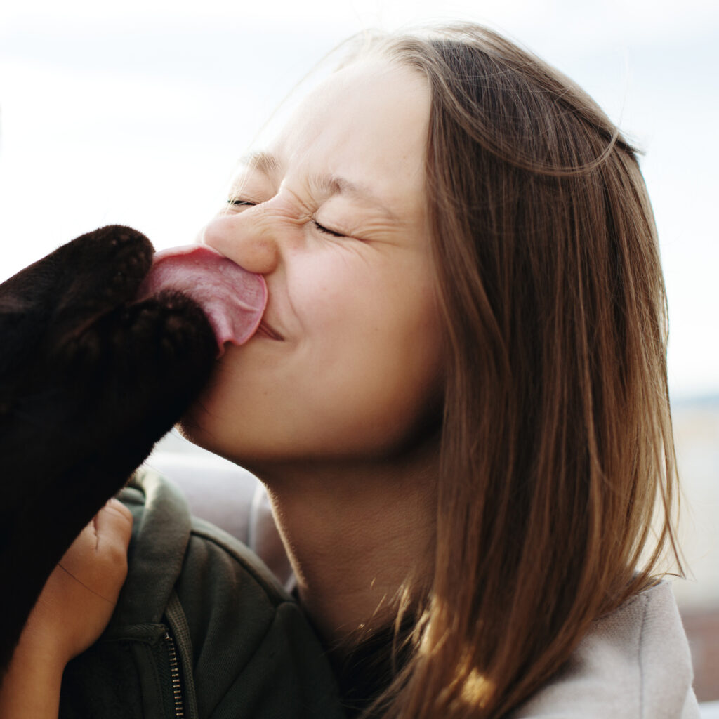 a woman with a black dog licking up her nose