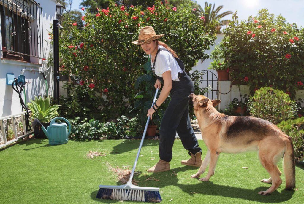 a woman is sweeping outside and a dog is watching her