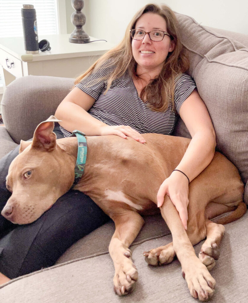 a woman wearing glasses and a striped shirt has a big tan dog laying on top of her lap